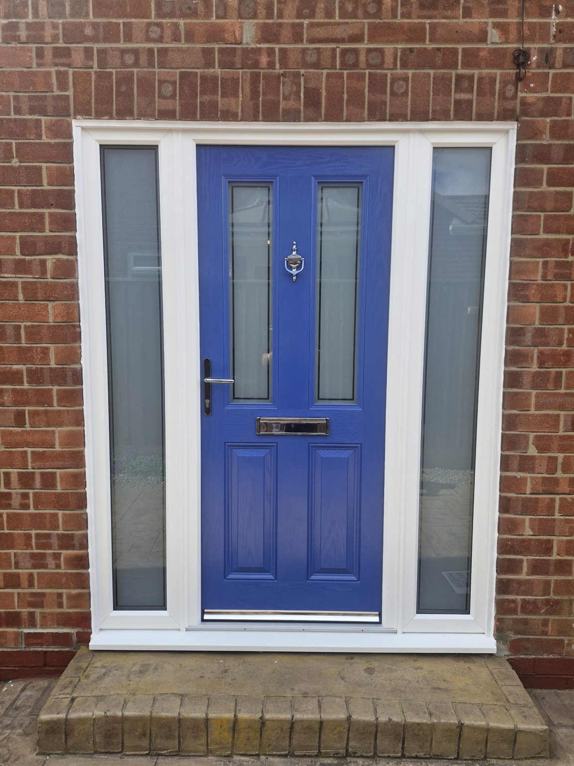 A blue front door with frosted glass sidelights in a white frame