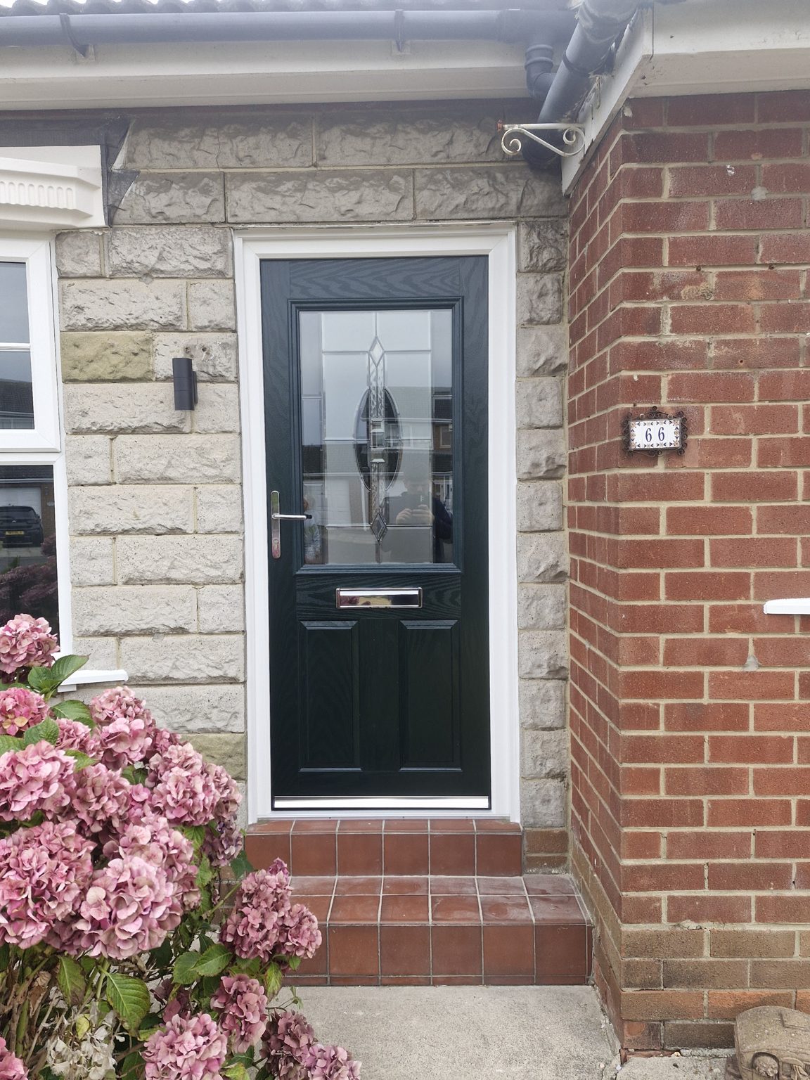 A black front door with a decorative glass panel, set in a stone and brick front