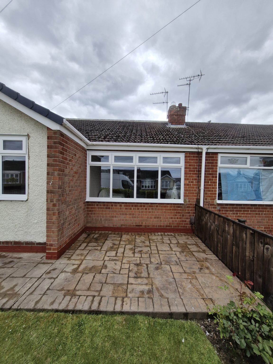 The back of a bungalow with new white windows above a paved patio