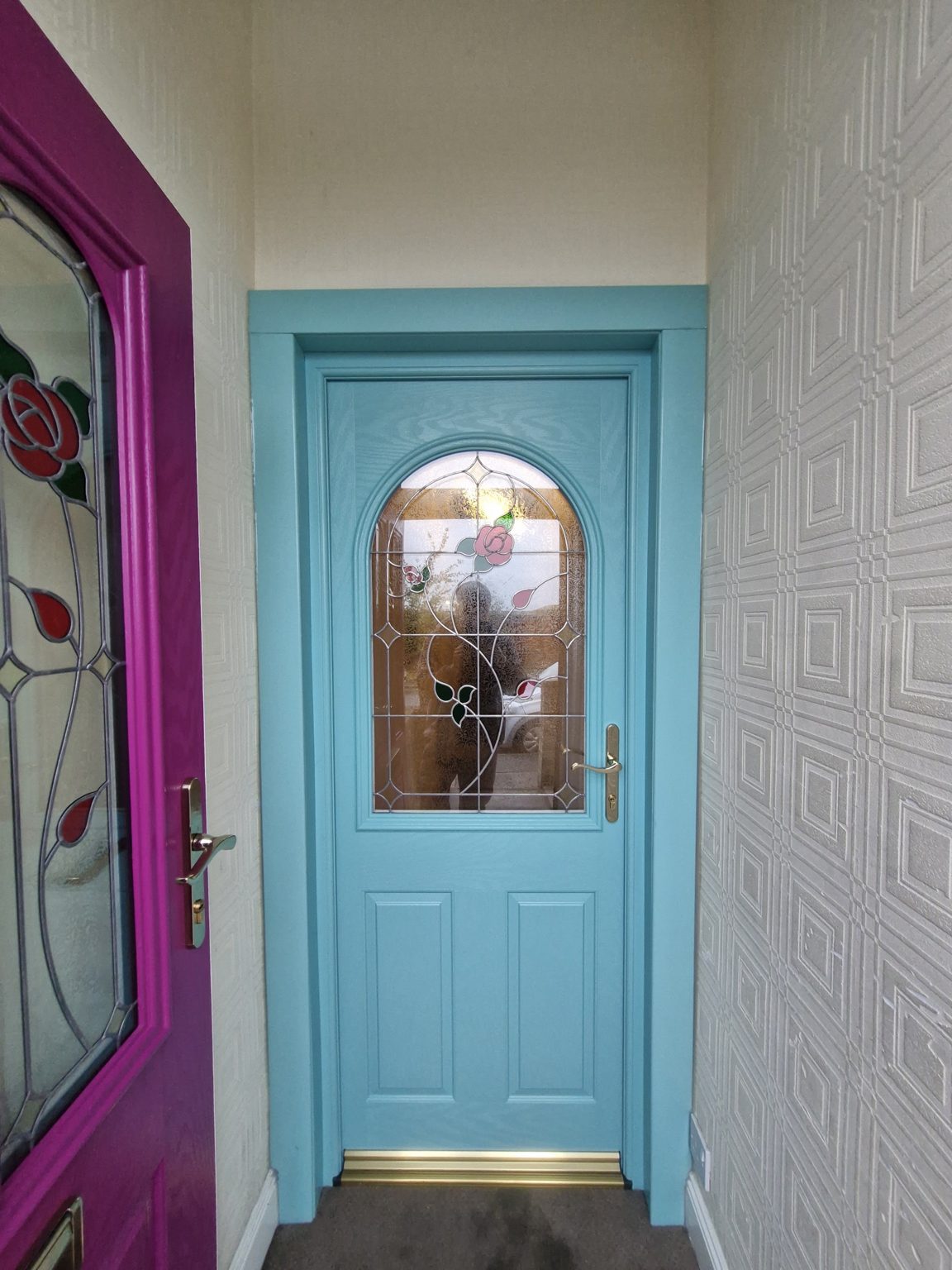 A teal front door with an arched leaded glass panel beside a magenta glazed door